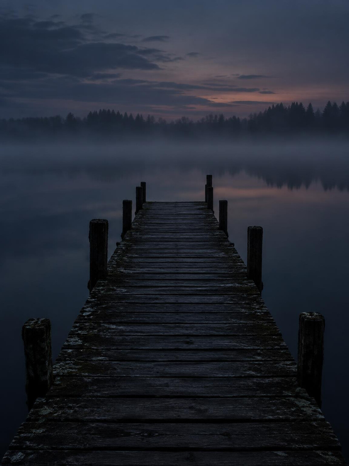 Empty wooden pier extending into dark still water at twilight